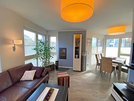 lichtdurchfluteter Wohnbereich mit Kamin, große Ledercouch, Couchtisch mit Hocker, Sideboard, Vitrine, Smart-TV mit Blu-Ray-Player sowie eine kleine Auswahl an Urlaubslektüre und CD`s