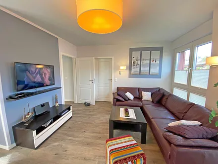 lichtdurchfluteter Wohnbereich mit Kamin, große Ledercouch, Couchtisch mit Hocker, Sideboard, Vitrine, Smart-TV mit Blu-Ray-Player sowie eine kleine Auswahl an Urlaubslektüre und CD`s