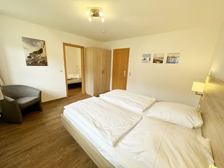 Schlafzimmer hell und modern eingerichtet mit Doppelbett, Komfortmatratzen (2x 0,90 m x 2,00 m), Nachttischkonsolen, Kleiderschrank und Verdunklungsgardinen