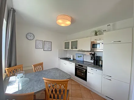 angrenzende Küchenzeile mit Geschirrspüler, Mikrowelle, Ceranfeld, Backofen, Kühlschrank mit Gefrierfach, Wasserkocher, Toaster, Kaffeemaschine und diverse Küchenutensilien