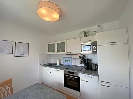 angrenzende Küchenzeile mit Geschirrspüler, Mikrowelle, Ceranfeld, Backofen, Kühlschrank mit Gefrierfach, Wasserkocher, Toaster, Kaffeemaschine und diverse Küchenutensilien