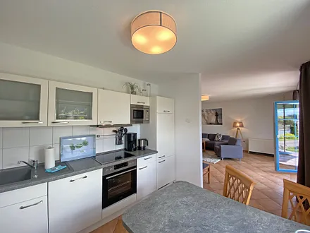 angrenzende Küchenzeile mit Geschirrspüler, Mikrowelle, Ceranfeld, Backofen, Kühlschrank mit Gefrierfach, Wasserkocher, Toaster, Kaffeemaschine und diverse Küchenutensilien