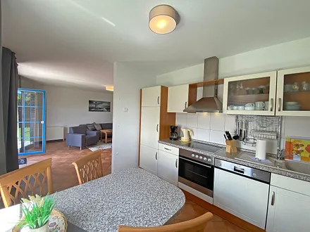 angrenzende Küchenzeile mit Geschirrspüler, Mikrowelle, Ceranfeld, Backofen, Kühlschrank mit Gefrierfach, Wasserkocher, Toaster, Kaffeemaschine und diversen Küchenutensilien 