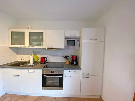 angrenzende Küchenzeile mit Geschirrspüler, Mikrowelle, 4 Zonen-Ceranfeld, Backofen, Kühlschrank mit Gefrierfach, Wasserkocher, Toaster, Kaffeemaschine und diversen Küchenutensilien 