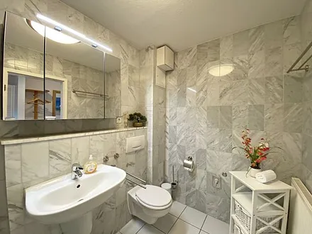 Badezimmer mit Marmorfliesen, Dusche mit flachem Einstieg, Waschtisch, Fön und WC