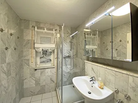 Badezimmer mit Marmorfliesen, Dusche mit flachem Einstieg, Waschtisch, Fön und WC