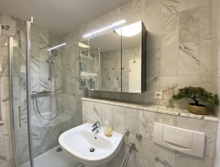 Badezimmer mit Marmorfliesen, Dusche mit flachem Einstieg, Waschtisch, Fön und WC