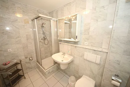 Badezimmer mit Marmorfliesen, Dusche, Kosmetikspiegel, Waschtisch, Fön und WC