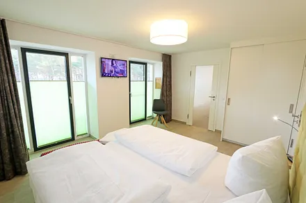 Schlafzimmer mit einem Doppelbett (1x 1,60 m x 2,00 m, 1x 0,90 m x 2,00 m ausziehbar auf 1,80 m und 1x 1,80 m x 2,00 m), Nachttischablagen mit Beleuchtung und USB Anschlüssen sowie Kleiderschränken