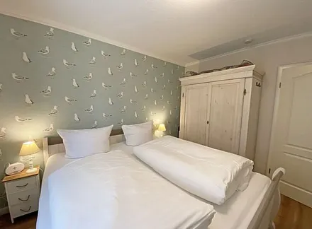 Schlafzimmer mit Doppelbett in Komforthöhe (1,80 m x 2,00 m), verstellbare Lattenroste, Nachtischablagen mit Lampen sowie ein zweitüriger Kleiderschrank