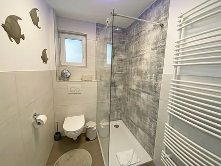 Tageslicht-Bad mit offener Glasdusche mit niedrigem Einstieg, Waschplatz, WC, Kosmetikspiegel, Fön, Handtuchtrockner sowie eine Fußbodenheizung