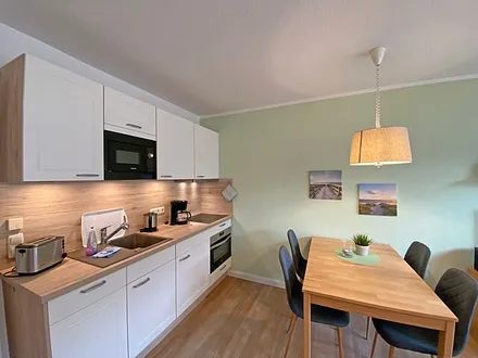 offene Küchenzeile mit Ceranfeld, Kompaktbackofen, Geschirrspüler, Mikrowelle, Spüle, Kühlschrank mit Gefrierfach und diverse Elektrokleingeräte und Küchenutensilien