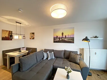 Wohnbereich mit gemütlicher Couch mit Ottomane, Couchtisch, Leselampe, kleines Highboard sowie TV-Board mit Smart-TV und DAB-Radio mit Bluetooth, USB und AUX 