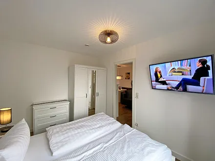 Schlafzimmer mit Doppelbett (1,60 m x 2,00 m, H3), Nachttischablagen, Kleiderschrank, Kommode, Smart-TV sowie Verdunklungsvorhang