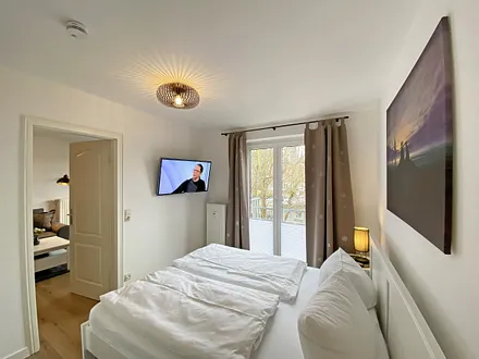 Schlafzimmer mit Doppelbett (1,60 m x 2,00 m, H3), Nachttischablagen, Kleiderschrank, Kommode, Smart-TV sowie Verdunklungsvorhang