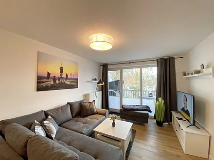 Wohnbereich mit gemütlicher Couch mit Ottomane, Couchtisch, Leselampe, kleines Highboard sowie TV-Board mit Smart-TV und DAB-Radio mit Bluetooth, USB und AUX