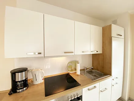 offene Küchenzeile mit Backofen, Cerankochfeld, Kühlschrank mit Gefrierfach, Geschirrspüler, Kaffeemaschine, Toaster sowie ein Wasserkocher