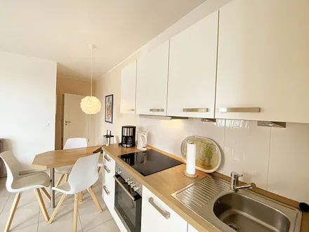 offene Küchenzeile mit Backofen, Cerankochfeld, Kühlschrank mit Gefrierfach, Geschirrspüler, Kaffeemaschine, Toaster sowie ein Wasserkocher