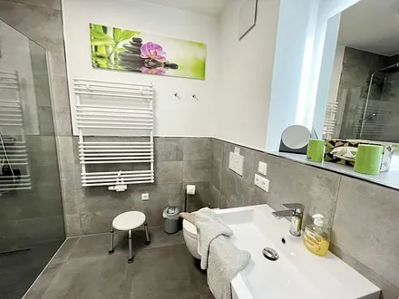 Badezimmer mit ebenerdiger Dusche, Waschtisch mit Spiegel, Handtuchheizkörper, Fön, Kosmetikspiegel, WC und Waschmaschine