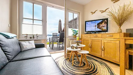 komfortabler Wohnbereich mit Couch, Couchtisch, Sessel, Stehlampe, Kommode mit Flachbild-TV