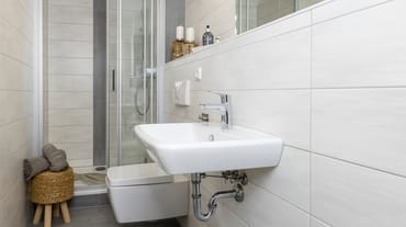 Badezimmer mit Dusche, WC, Fön sowie ein Waschplatz mit dazugehörigem Spiegel