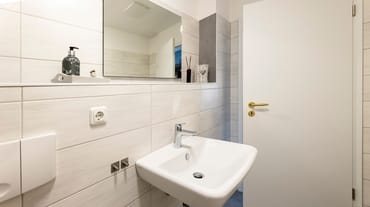 Badezimmer mit Dusche, WC, Fön sowie ein Waschplatz mit dazugehörigem Spiegel