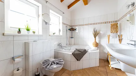 Badezimmer mit geräumiger Eck-Badewanne, WC, Fön, Kosmetikspiegel und ein Doppelwaschplatz mit dazugehörigem Spiegel