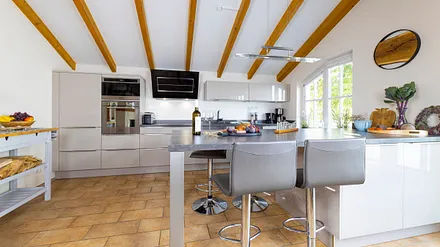 offene Küchenzeile mit Spülmaschine, Backofen, Dunstabzugshaube, Induktionsfeld, Mikrowelle, Kühlschrank mit Eisfach, Wasserkocher, Kaffemaschine, Toaster und allerlei Küchenkleingeräte