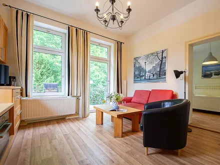 Der Wohnbereich mit Couchgarnitur und Küchenzeile sowie einem Zugang zum möblierten Balkon