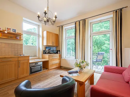 Der Wohnbereich mit Couchgarnitur und Küchenzeile sowie einem Zugang zum möblierten Balkon