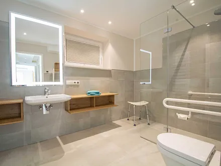 Das erste großzügige Bad mit Regenwaldusche und Haltegriffen an WC und in der Dusche sowie unterfahrbares Waschbecken