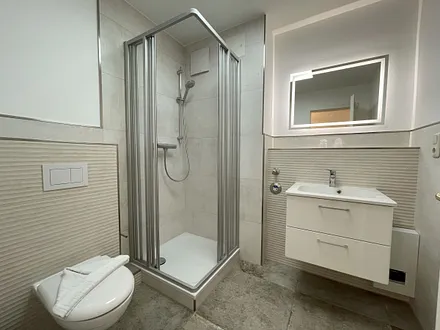 Badezimmer mit ebenerdiger Dusche, WC, Fön sowie ein Waschplatz mit Unterschrank