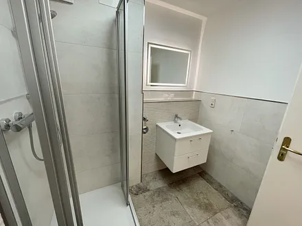 Badezimmer mit ebenerdiger Dusche, WC, Fön sowie ein Waschplatz mit Unterschrank