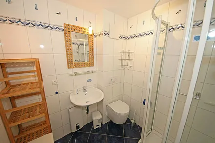 Badezimmer mit flacher Dusche, Waschplatz, WC, Fön, Kosmetikspiegel und Handtuchheizkörper