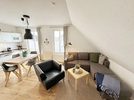 Wohnbereich mit bequemer Eckcouch, Couchtisch, Sessel, Stehlampe, 32-Zoll-Smart-TV, Bluetooth-Radio, Sideboard sowie eine Spielesammlung und kleine Auswahl an Büchern