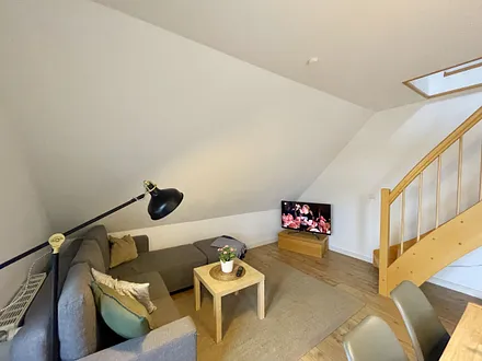 Wohnbereich mit bequemer Eckcouch, Couchtisch, Sessel, Stehlampe, 32-Zoll-Smart-TV, Bluetooth-Radio, Sideboard sowie eine Spielesammlung und kleine Auswahl an Büchern