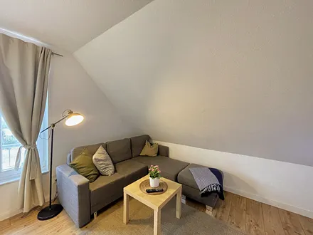 Wohnbereich mit bequemer Eckcouch, Couchtisch, Sessel, Stehlampe, 32-Zoll-Smart-TV, Bluetooth-Radio, Sideboard sowie eine Spielesammlung und kleine Auswahl an Büchern