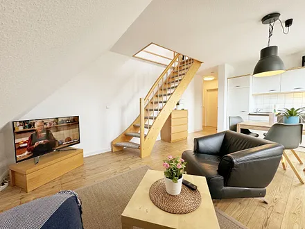 Wohnbereich mit bequemer Eckcouch, Couchtisch, Sessel, Stehlampe, 32-Zoll-Smart-TV, Bluetooth-Radio, Sideboard sowie eine Spielesammlung und kleine Auswahl an Büchern