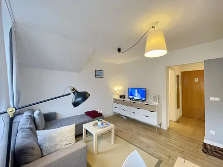 Wohnzimmer mit bequemer Eckcouch, Couchtisch, Stehlampe, 32-Zoll-Smart-TV, Bluetooth-Radio, Sideboard sowie eine Spielesammlung und kleine Auswahl an Büchern