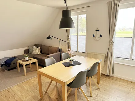 Wohnbereich mit bequemer Eckcouch, Couchtisch, Sessel, Stehlampe, 55-Zoll-Smart-TV, Bluetooth-Radio, Sideboard sowie eine Spielesammlung und kleine Auswahl an Büchern