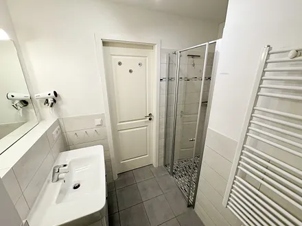 Badezimmer mit ebenerdiger Dusche, Waschbecken, WC, Handtuchheizkörper und einen Fön