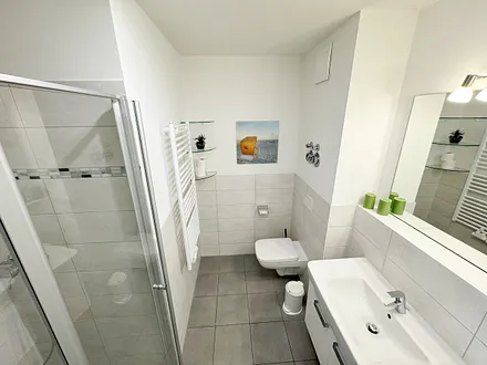 Badezimmer mit ebenerdiger Dusche, Waschbecken, WC, Handtuchheizkörper und einen Fön