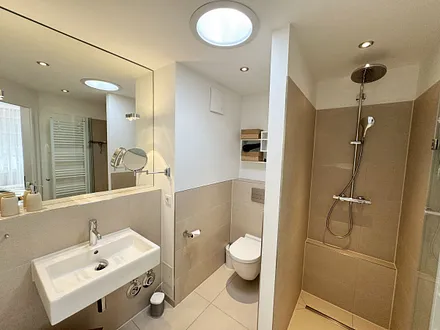 Badezimmer mit bodentiefer Echtglasdusche, Kosmetikspiegel, Fön, Handtuchtrockner sowie einer Lichtkuppel, die diesen Raum schon ab dem frühen Morgen erhellt