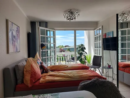 Der schöne Wohnschlafraum hat eine große Fensterfront zum Balkon. TV und kostenfreies WLAn sind vorhanden.