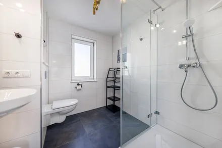 Das moderne Bad mit Echtglasdusche, WC, Fön und Fenster.