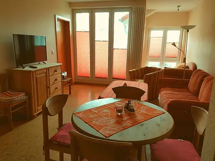 Blick Wohnzimmer Richtung Balkon mit großer Balkontür und wintergartenähnlichen Anbau mit Couch, Alle Fenster verfügen über hochwertige Plisees 