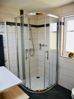 Badezimmer mit Eckrunddusche und Handtuchtrockner über Fußbodenheizung