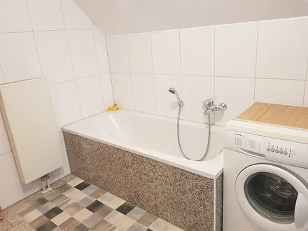 Eine Badewanne lädt zum Relaxen ein, das Luxusbadezimmer verfügt über einen modernen Natursteinboden