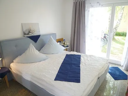 Modernes Schlafzimmer mit chicem blauen Bett, doppelflüglige Tür zur Terrasse