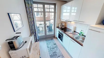 Die voll eingerichtete Küche der Wohnung Kuckuck, dahinter der Balkon, von dem aus Sie das Achterwasser sehen können.